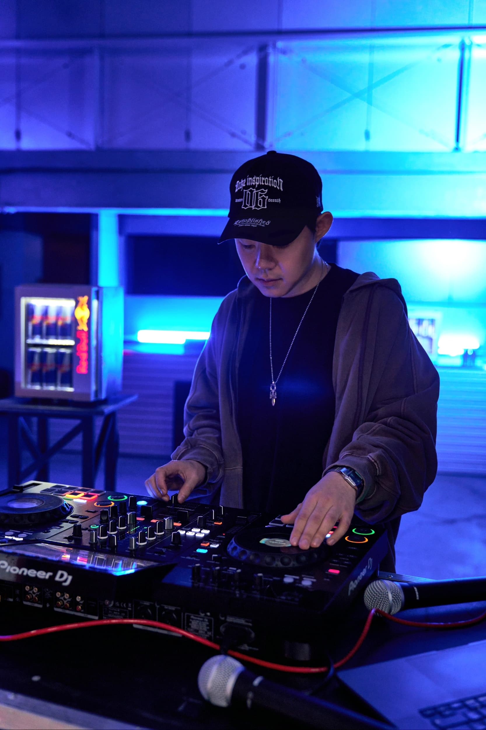DJ KNDRX — 블루 네온 아래 부스에서 디제잉 중